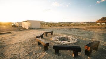 A desert landscape with a fire pit and benches, a white building, and a clear sky.