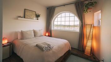 A bedroom with a large bed, a window with curtains, a map on the wall, and a plant.