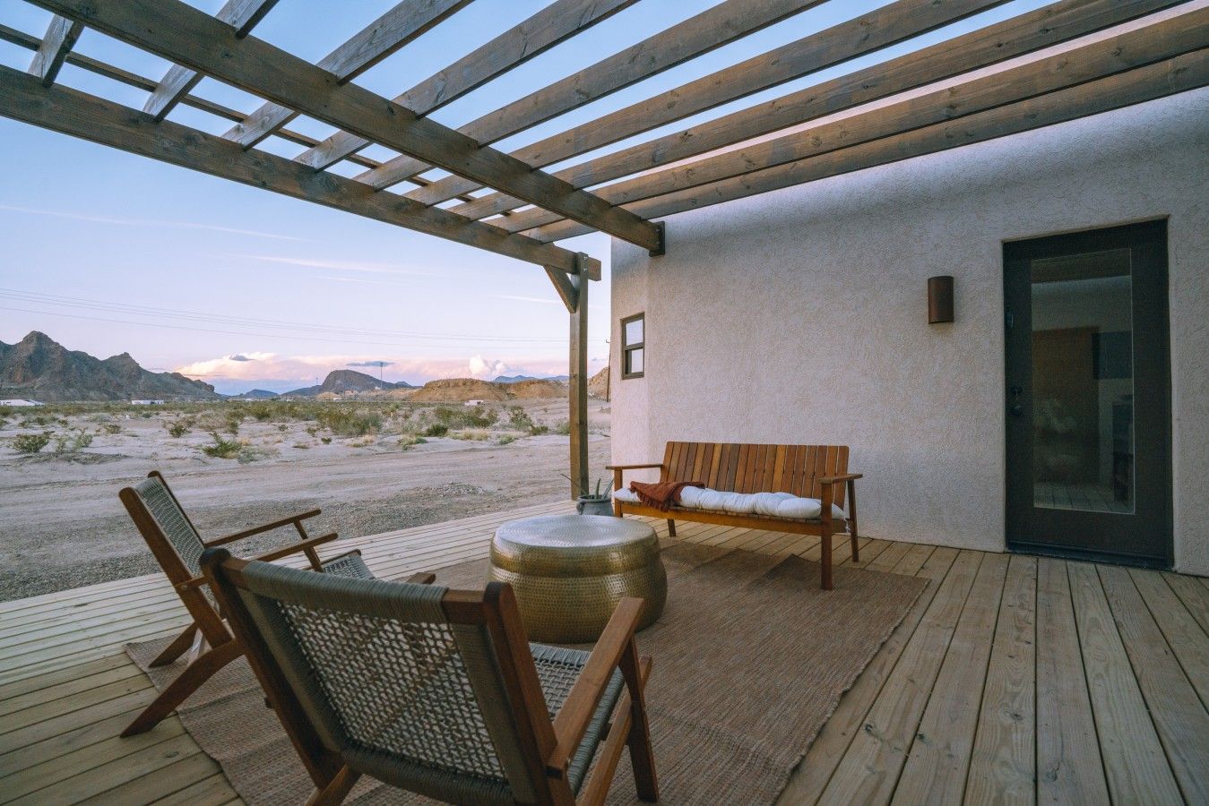 Eine Holzterrasse mit einer Bank, Stühlen und einem runden Tisch, mit Blick auf eine Wüstenlandschaft.