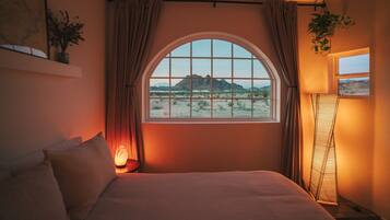 Una camera da letto con un'ampia finestra ad arco, un letto, un comodino con una lampada e una lampada da terra.