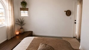 Een slaapkamer met een bed, een raam, een deur en een hangplant.