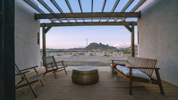 Eine Terrasse im Freien mit einer Pergola, zwei Holzstühlen, einem runden Tisch und Blick auf eine gebirgige Landschaft.