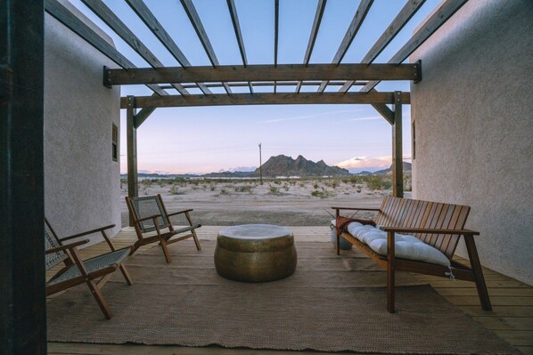 An outdoor patio with a pergola, two wooden chairs, a round table, and a view of a mountainous landscape.