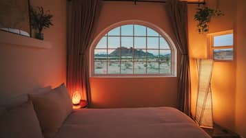Ein Schlafzimmer mit einem großen Bogenfenster, einem Bett, einem Nachttisch mit Lampe und einer Stehlampe.