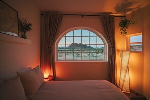 A bedroom with a large arched window, a bed, a bedside table with a lamp, and a floor lamp.