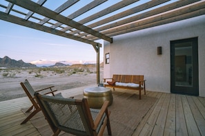En træterrasse med bænk og stole, et rundt bord og udsigt over et ørkenlandskab.