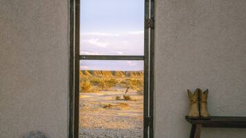 A room with a wooden floor, a bench, a pair of boots, and a large arched doorway leading to a landscape view.