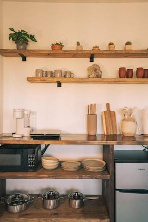 Une cuisine équipée d’étagères en bois, d’une machine à café, d’un four à micro-ondes, d’un réfrigérateur Galanz et de divers ustensiles de cuisine.