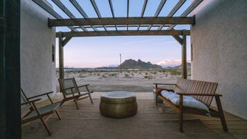An outdoor patio with a pergola, two wooden chairs, a round table, and a view of a mountainous landscape.