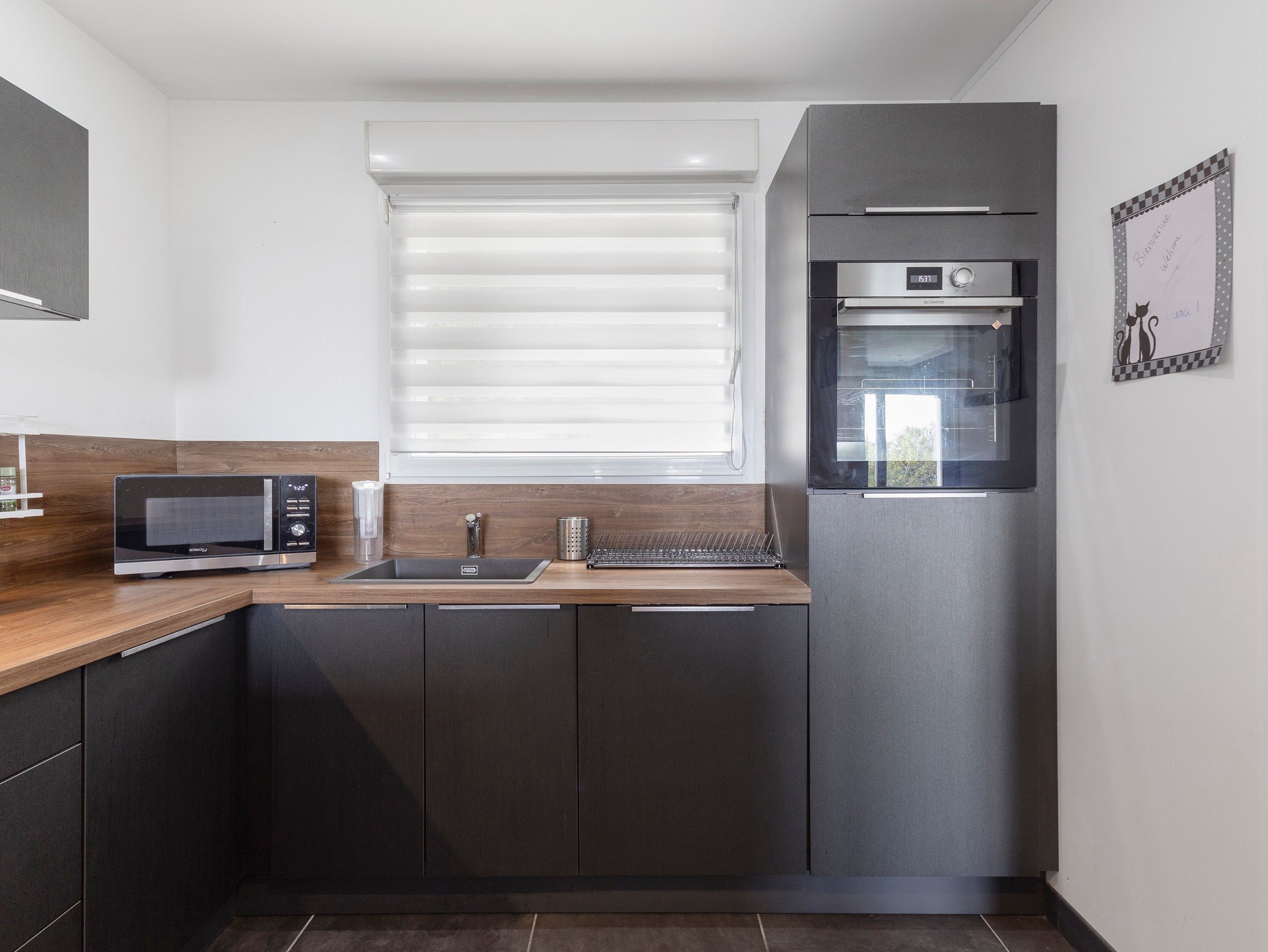 Una cocina moderna con microondas integrado, un lavamanos de acero inoxidable y un refrigerador.