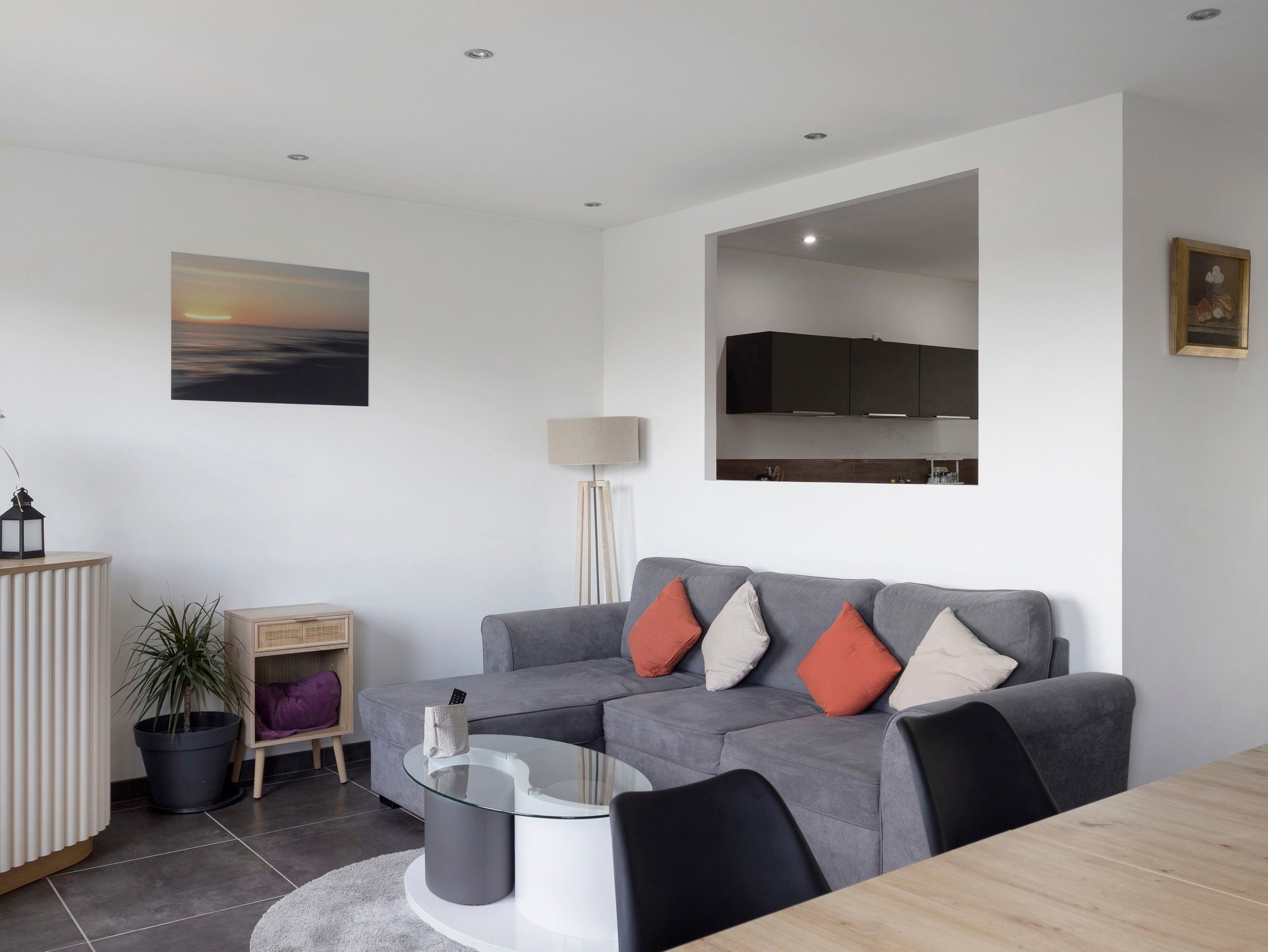 Un salon moderne avec un canapé gris, une table basse en verre et un téléviseur à écran plat fixé au mur.
