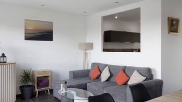 Un salon moderne avec un canapé gris, une table basse en verre et un téléviseur à écran plat fixé au mur.