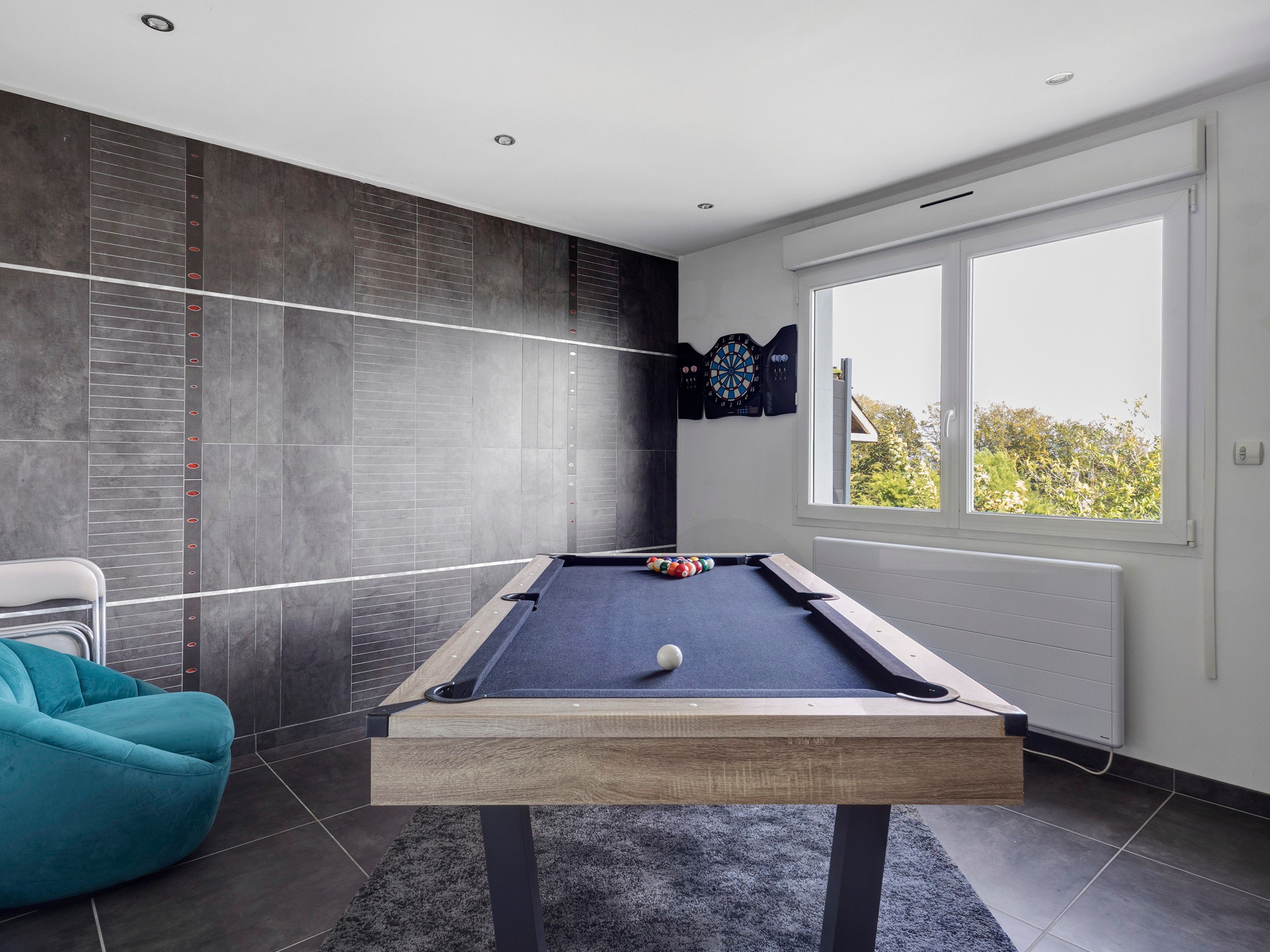 Ein modernes Zimmer mit Poolbillard, Dartscheibe und Blick durch ein großes Fenster.