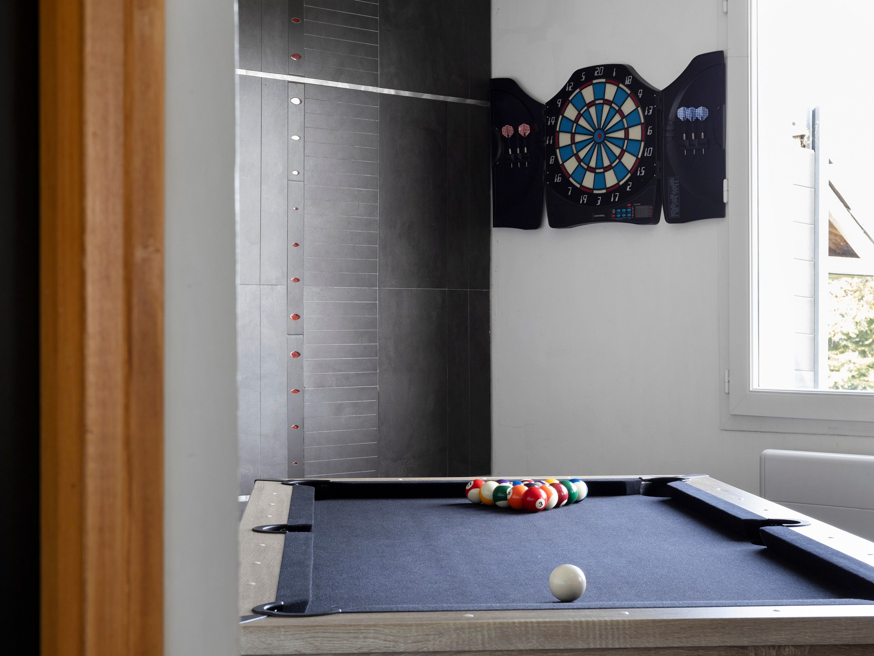 A billiards table with a dartboard and a clock on the wall.