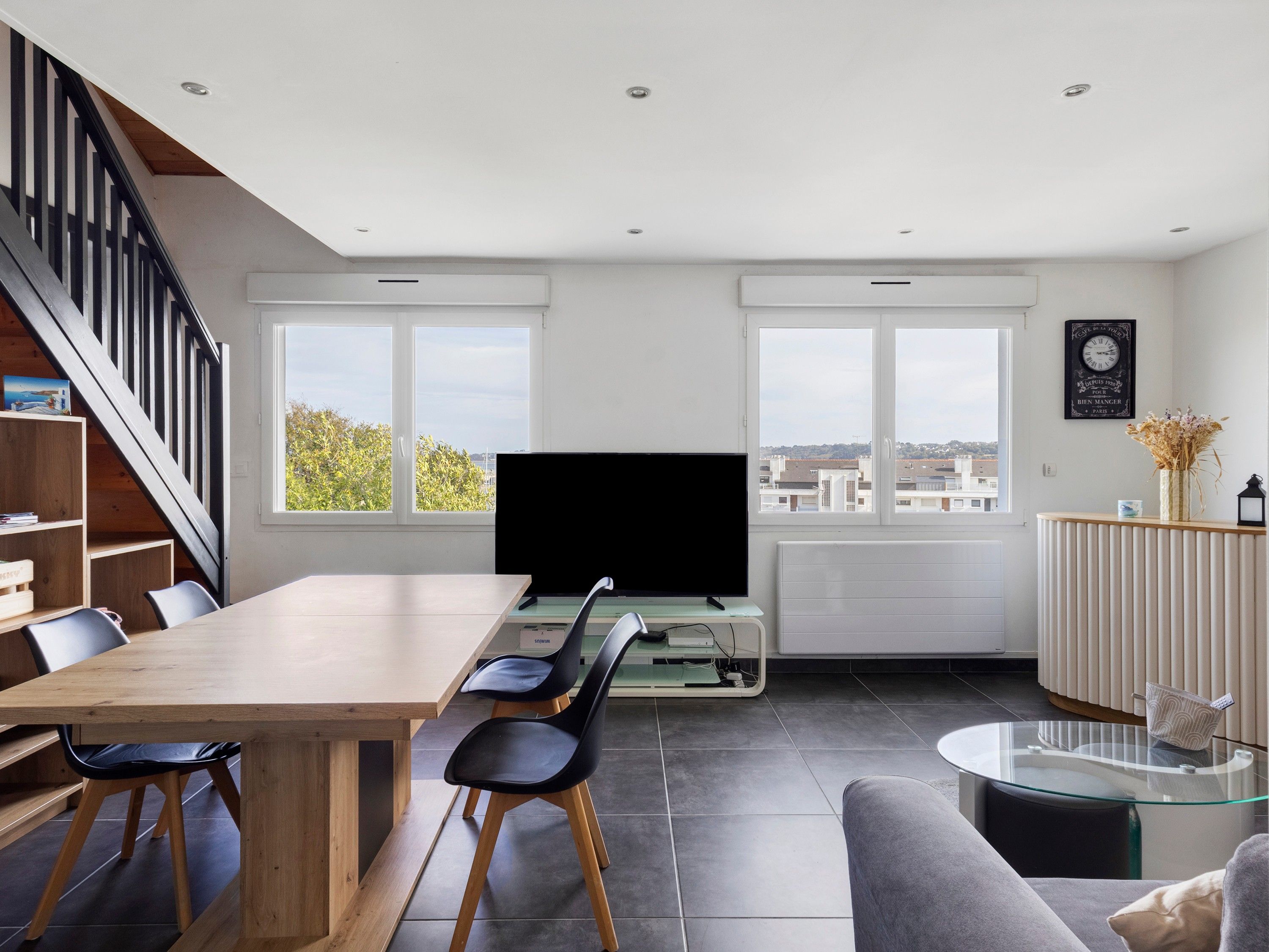 Una sala de estar moderna con una mesa de comedor de madera, sillas negras, un televisor de pantalla plana, una mesa de centro de vidrio y un sofá.