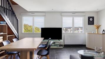 Una sala de estar moderna con una mesa de comedor de madera, sillas negras, un televisor de pantalla plana, una mesa de centro de vidrio y un sofá.