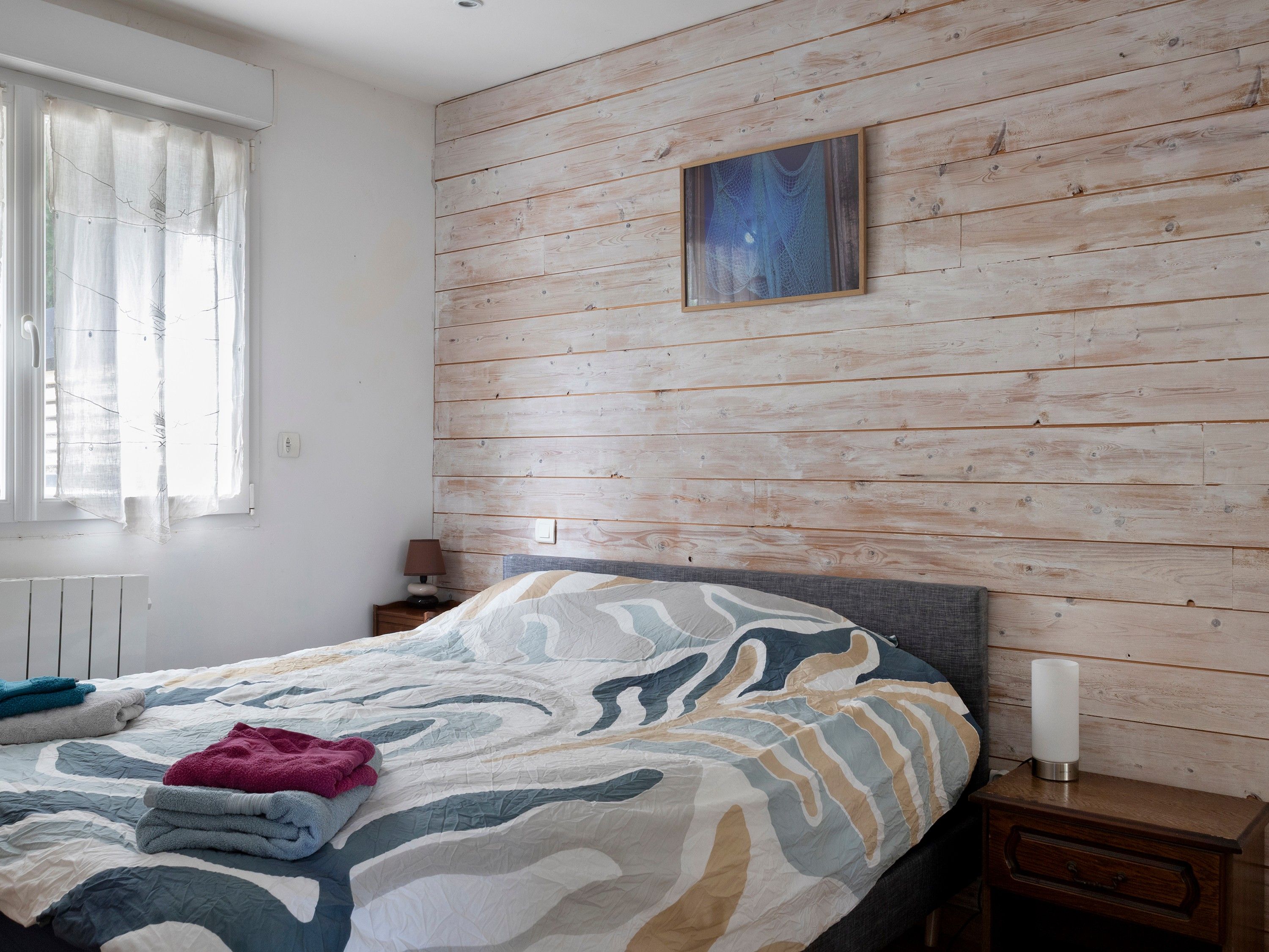 Une chambre à coucher avec un lit, une table de chevet, une lampe et une fenêtre avec des rideaux.