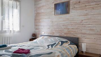Une chambre à coucher avec un lit, une table de chevet, une lampe et une fenêtre avec des rideaux.