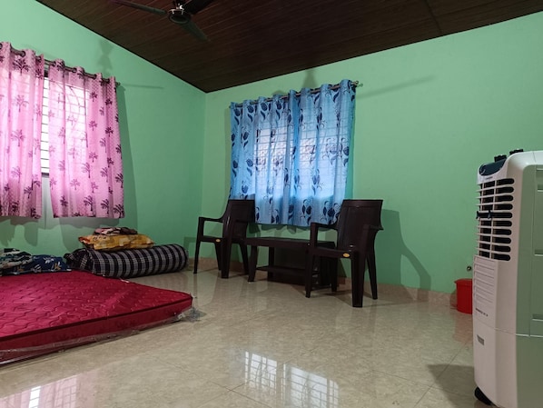 A room with a bed, two chairs, a table, a ceiling fan, and an air conditioner.