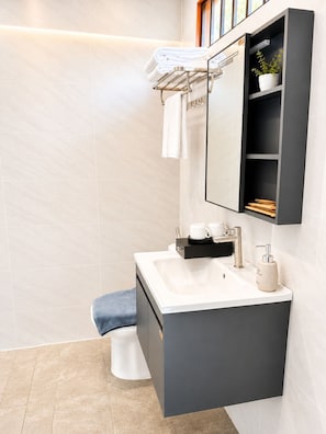 A modern bathroom with a white sink, a towel rack, a mirror, and a shelf with toiletries.