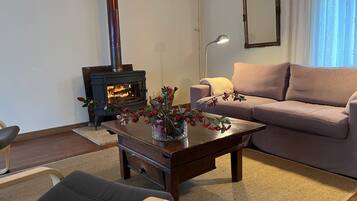 Ein Wohnzimmer mit einer Couch, einem Couchtisch mit Blumen, einem Holzstuhl, einem Kamin und einer Lampe.