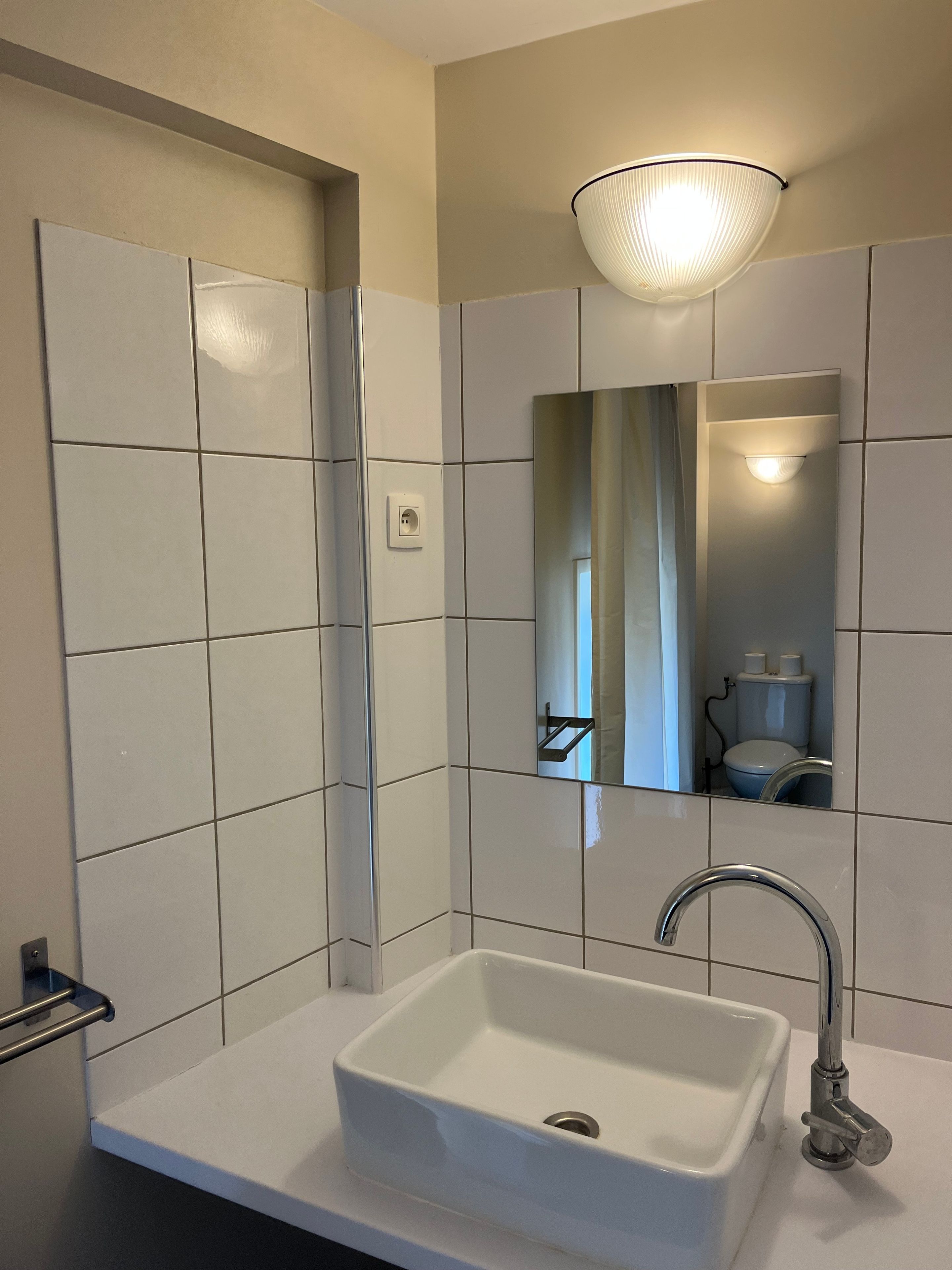 A bathroom with a white sink, a mirror, and a wall-mounted light fixture.