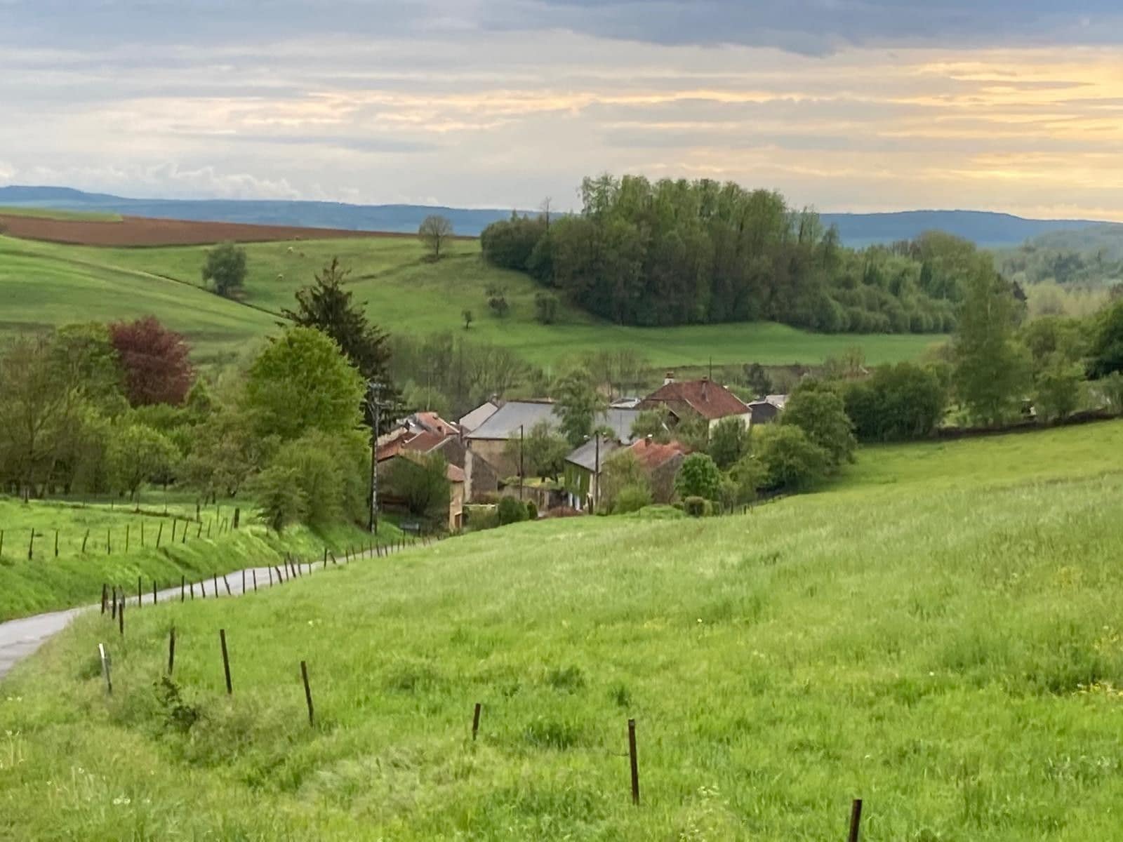 A rural landscape with rolling hills, a fenced vineyard, and a cluster of houses with red roofs.
