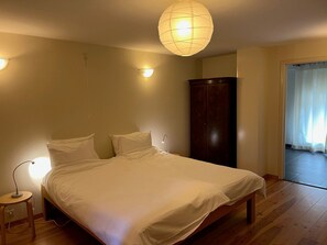 A bedroom with a bed, bedside lamps, a wardrobe, and a door leading to another room.
