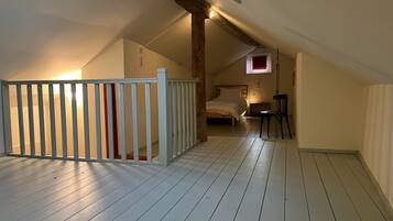 Une pièce avec un plafond en pente, un lit, une chaise, une table de chevet et une petite fenêtre.