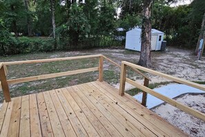 A wooden deck with a railing, surrounded by trees and a small shed.