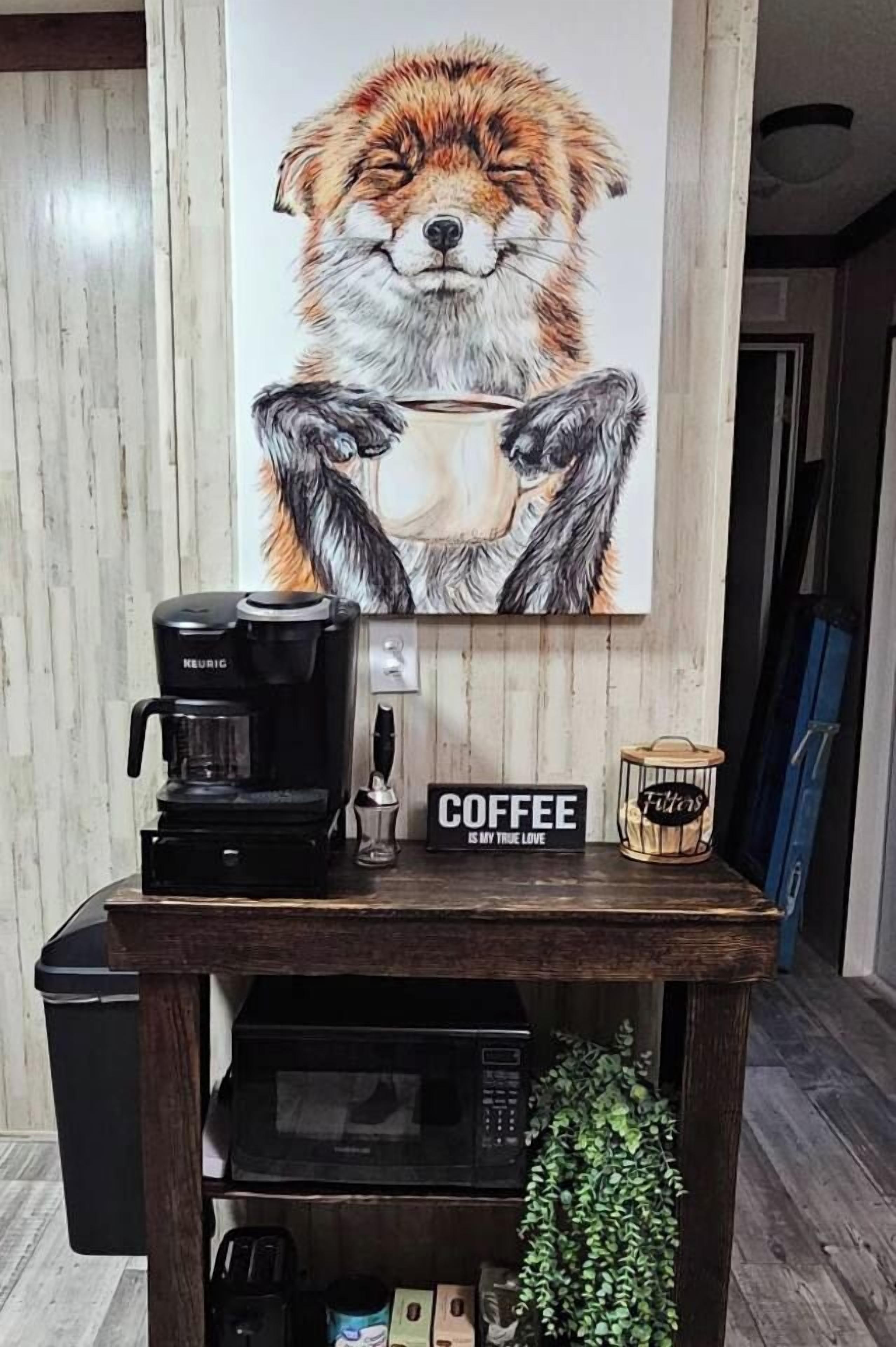 A coffee maker on a wooden table with a coffee cup and a sign that reads 'COFFEE IS MY TRUE LOVE.'