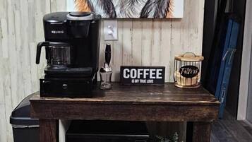A coffee maker on a wooden table with a coffee cup and a sign that reads 'COFFEE IS MY TRUE LOVE.'