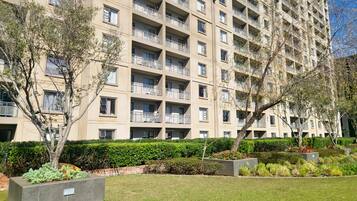 Un edificio residencial de varios pisos con balcones, rodeado de céspedes y árboles bien cuidados.