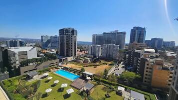 Un edificio residencial de gran altura con piscina en la azotea y jardín ajardinado.