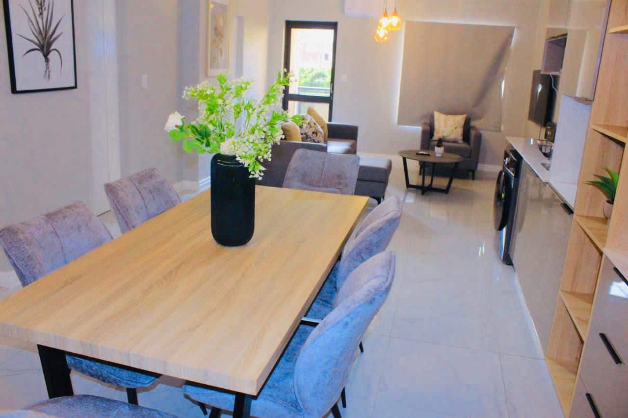 Un comedor moderno con una mesa y sillas de madera, un jarrón con flores y vista al salón.