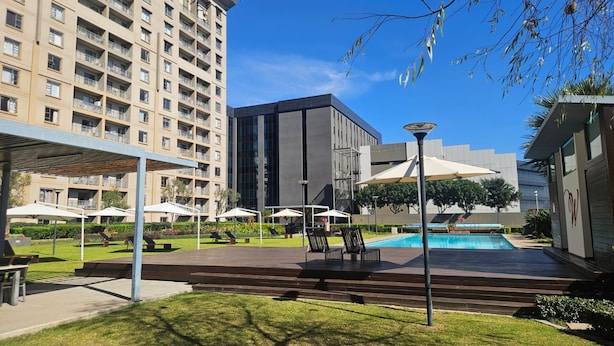 A hotel courtyard with a swimming pool, outdoor seating, and a modern building. - Sandton Westpoint Luxury Apartments - 7 (Sandton)