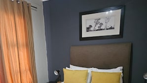 A neatly made bed with white and yellow pillows, a grey throw blanket, and rolled white towels on the side. - Sandton Westpoint Luxury Apartments - 7 (Sandton)