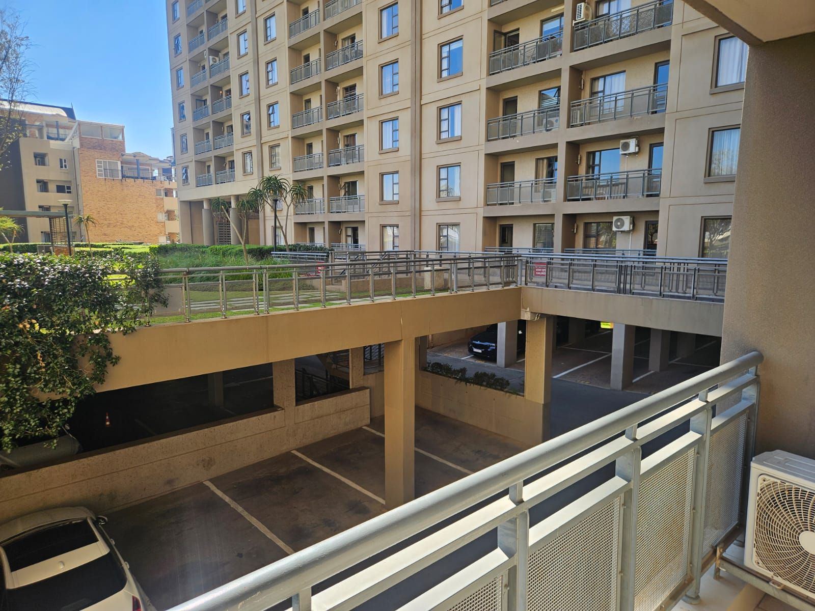 Una estructura de estacionamiento de varios pisos con un puente peatonal, rodeada de edificios con balcones.