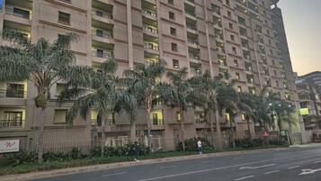 Un edificio residencial de varios pisos con balcones, una entrada vigilada y una calle en frente.