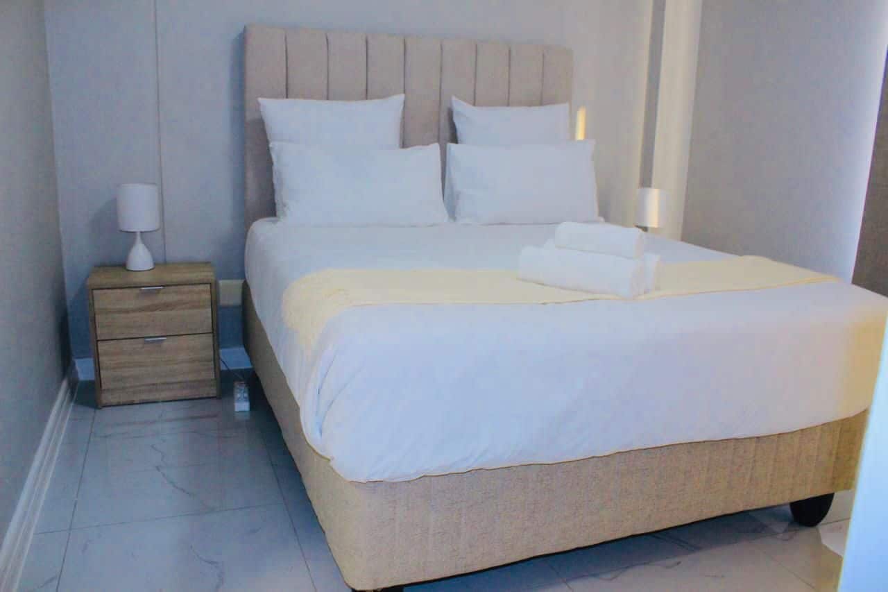 Una cama bien hecha con sábanas blancas y un cabecero color beige en una habitación de hotel.
