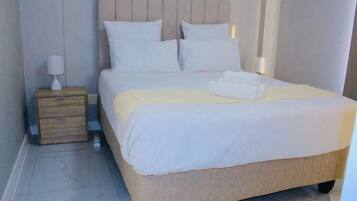 Una cama bien hecha con sábanas blancas y un cabecero color beige en una habitación de hotel.