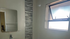 A modern bathroom with a freestanding bathtub, a wall-mounted sink, and a window providing natural light. - Sandton Westpoint Luxury Apartments - 7 (Sandton)
