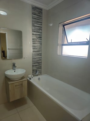 A modern bathroom with a freestanding bathtub, a wall-mounted sink, and a window providing natural light. - Sandton Westpoint Luxury Apartments - 7 (Sandton)