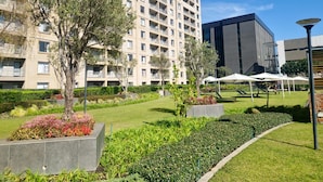 A modern hotel with a large building, a courtyard with greenery, and outdoor seating. - Sandton Westpoint Luxury Apartments - 7 (Sandton)