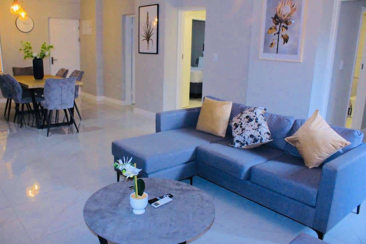 Una sala de estar moderna con un sofá azul, una mesa redonda de centro con una planta, y un comedor con una mesa y sillas.