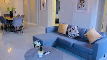Una sala de estar moderna con un sofá azul, una mesa redonda de centro con una planta, y un comedor con una mesa y sillas.
