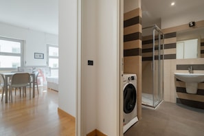 Un apartamento moderno con lavadora, cabina de ducha de vidrio y comedor con sillas.