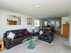 A living room with a glass coffee table, two leather sofas, a mirror, and a kitchen in the background. - 2 Inglewood Apartments (Dartmouth)
