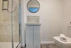 Ein Badezimmer mit Duschkabine aus Glas, einem weißen Waschbecken mit Spiegel darüber und einer Toilette.