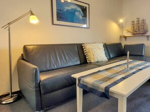A modern living room with a leather sofa, a white coffee table, a floor lamp, a framed artwork, and a ship model on a shelf. - Holiday Apartment With 1 Bedroom (Wyk auf Foehr)
